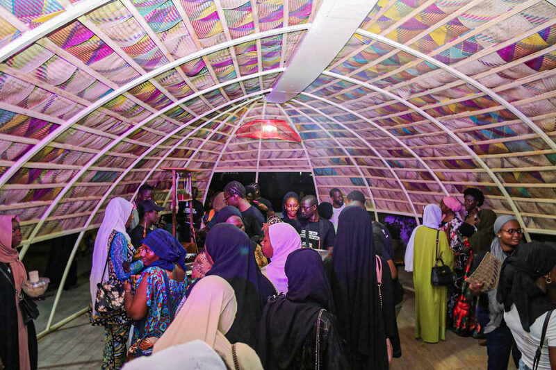 A crowd gathered at night under the lit, colorful fan ceiling of Le Nid de Bamako.